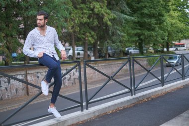 Güzel, koyu saçlı, metal parmaklıklara yaslanmış bir adam. Yüksek kalite fotoğraf