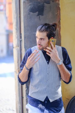 Gömleği ve yeleği olan güzel siyah saçlı İtalyan adam sokakta sigara içiyor. Yüksek kalite fotoğraf