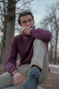 Güz mevsiminde koyu renk saçlı güzel bir İtalyan çocuğu koyu kırmızı kazağıyla bankta oturuyor. Yüksek kalite fotoğraf