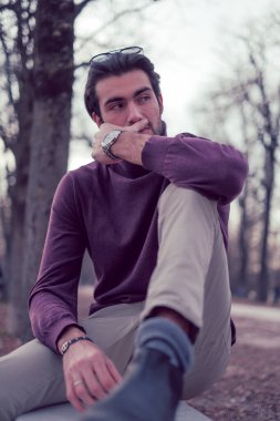 Güz mevsiminde koyu renk saçlı güzel bir İtalyan çocuğu koyu kırmızı kazağıyla bankta oturuyor. Yüksek kalite fotoğraf