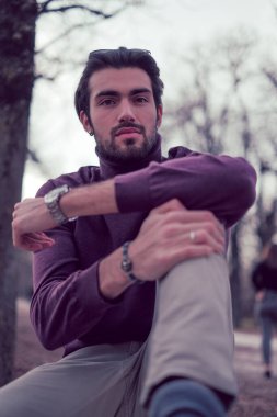 Güz mevsiminde koyu renk saçlı güzel bir İtalyan çocuğu koyu kırmızı kazağıyla bankta oturuyor. Yüksek kalite fotoğraf