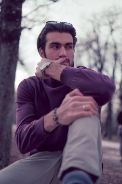 Güz mevsiminde koyu renk saçlı güzel bir İtalyan çocuğu koyu kırmızı kazağıyla bankta oturuyor. Yüksek kalite fotoğraf