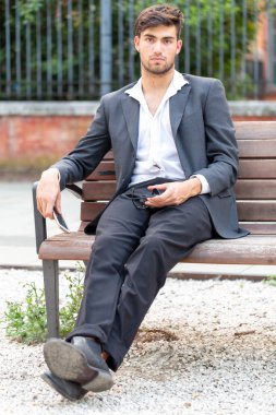 Ceketi ve pantolonu bankta oturan zarif siyah saçlı İtalyan çocuk. Yüksek kalite fotoğraf