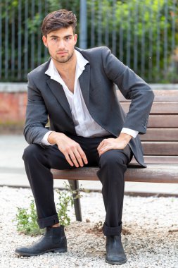 Ceketi ve pantolonu bankta oturan zarif siyah saçlı İtalyan çocuk. Yüksek kalite fotoğraf