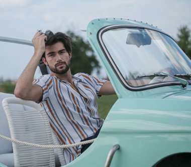 İtalyan esmer çocuk, klasik bir arabanın yanında poz veriyor. Autobianchi Bianchina Spiaggina. Yüksek kalite fotoğraf