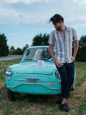 İtalyan esmer çocuk, klasik bir arabanın yanında poz veriyor. Autobianchi Bianchina Spiaggina. Yüksek kalite fotoğraf
