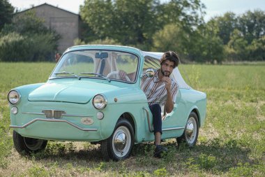 İtalyan esmer çocuk, klasik bir arabanın yanında poz veriyor. Autobianchi Bianchina Spiaggina. Yüksek kalite fotoğraf