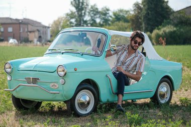 İtalyan esmer çocuk, klasik bir arabanın yanında poz veriyor. Autobianchi Bianchina Spiaggina. Yüksek kalite fotoğraf