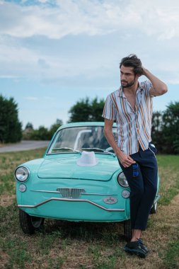 İtalyan esmer çocuk, klasik bir arabanın yanında poz veriyor. Autobianchi Bianchina Spiaggina. Yüksek kalite fotoğraf