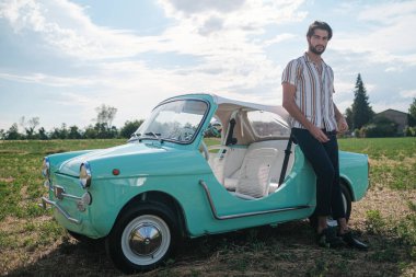 İtalyan esmer çocuk, klasik bir arabanın yanında poz veriyor. Autobianchi Bianchina Spiaggina. Yüksek kalite fotoğraf