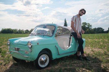 İtalyan esmer çocuk, klasik bir arabanın yanında poz veriyor. Autobianchi Bianchina Spiaggina. Yüksek kalite fotoğraf