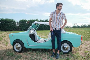 İtalyan esmer çocuk, klasik bir arabanın yanında poz veriyor. Autobianchi Bianchina Spiaggina. Yüksek kalite fotoğraf