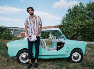 İtalyan esmer çocuk, klasik bir arabanın yanında poz veriyor. Autobianchi Bianchina Spiaggina. Yüksek kalite fotoğraf