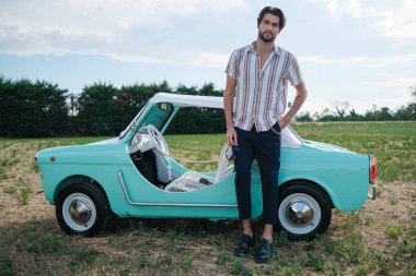 İtalyan esmer çocuk, klasik bir arabanın yanında poz veriyor. Autobianchi Bianchina Spiaggina. Yüksek kalite fotoğraf