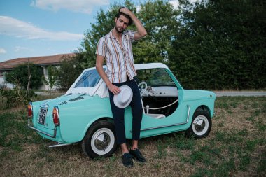 İtalyan esmer çocuk, klasik bir arabanın yanında poz veriyor. Autobianchi Bianchina Spiaggina. Yüksek kalite fotoğraf