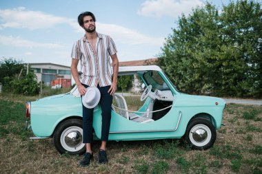 İtalyan esmer çocuk, klasik bir arabanın yanında poz veriyor. Autobianchi Bianchina Spiaggina. Yüksek kalite fotoğraf