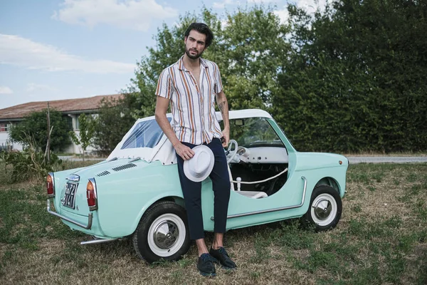 İtalyan esmer çocuk, klasik bir arabanın yanında poz veriyor. Autobianchi Bianchina Spiaggina. Yüksek kalite fotoğraf