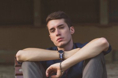 Güzel, koyu saçlı bir çocuk bankta bacak bacak bacak üstüne atmış. Yüksek kalite fotoğraf