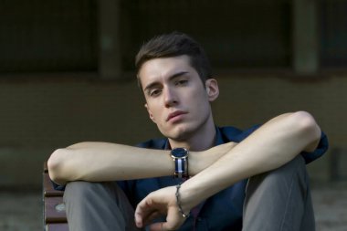 Güzel, koyu saçlı bir çocuk bankta bacak bacak bacak üstüne atmış. Yüksek kalite fotoğraf