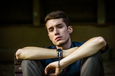 Güzel, koyu saçlı bir çocuk bankta bacak bacak bacak üstüne atmış. Yüksek kalite fotoğraf