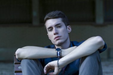 Güzel, koyu saçlı bir çocuk bankta bacak bacak bacak üstüne atmış. Yüksek kalite fotoğraf