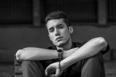 Güzel, koyu saçlı bir çocuk bankta bacak bacak bacak üstüne atmış. Yüksek kalite fotoğraf