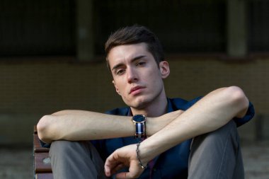 Güzel, koyu saçlı bir çocuk bankta bacak bacak bacak üstüne atmış. Yüksek kalite fotoğraf