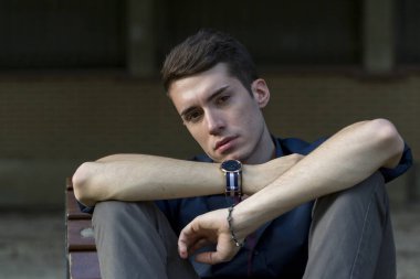 Güzel, koyu saçlı bir çocuk bankta bacak bacak bacak üstüne atmış. Yüksek kalite fotoğraf