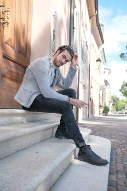 Ceketli, siyah saçlı yakışıklı İtalyan bir adam merdivende oturuyor. Yüksek kalite fotoğraf