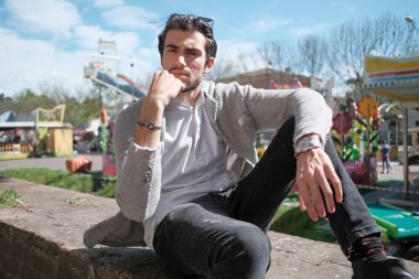 Yakışıklı, siyah saçlı, ceketli, güneşli bir günde alçak duvarda oturan adam. Yüksek kalite fotoğraf