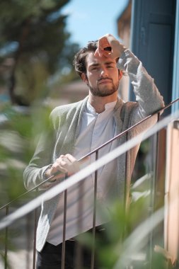 handsome Italian dark-haired guy leaning against railing in sunny day. High quality photo