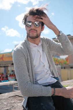 Yakışıklı, siyah saçlı, ceketli, güneşli bir günde alçak duvarda oturan adam. Yüksek kalite fotoğraf