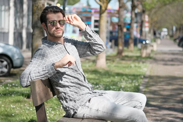 Yakışıklı, siyah saçlı, güneş gözlüklü, bankta oturan adam. Yüksek kalite fotoğraf