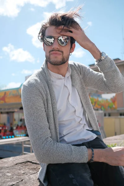 Yakışıklı, siyah saçlı, ceketli, güneşli bir günde alçak duvarda oturan adam. Yüksek kalite fotoğraf