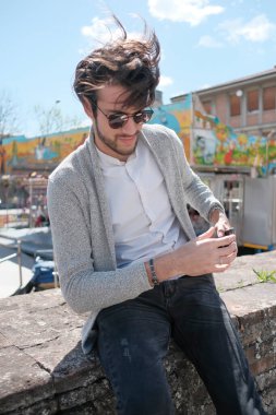 Yakışıklı, siyah saçlı, ceketli, güneşli bir günde alçak duvarda oturan adam. Yüksek kalite fotoğraf