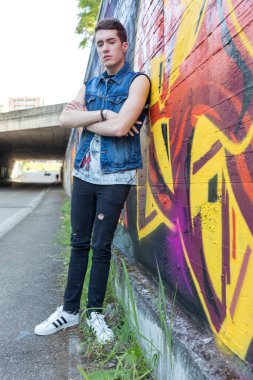 beautiful dark brown street style guy with jeans jacket in a street with graffiti. High quality photo