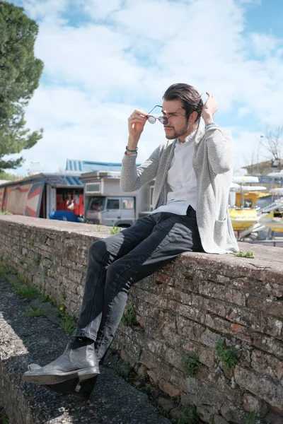 Yakışıklı, siyah saçlı, ceketli, güneşli bir günde alçak duvarda oturan adam. Yüksek kalite fotoğraf