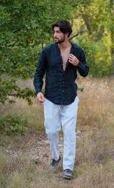 Kuru çimenlerde gömleği olan yakışıklı, siyah saçlı bir İtalyan. Yüksek kalite fotoğraf