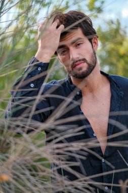 Kuru çimenlerde gömleği olan yakışıklı, siyah saçlı bir İtalyan. Yüksek kalite fotoğraf