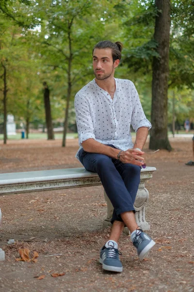 stock image handsome Italian dark-haired boy with shirt sitting on the bench in the Ducale park in Parma. High quality photo