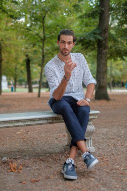 Parma 'daki Ducale parkındaki bankta oturan siyah tişörtlü yakışıklı İtalyan çocuk. Yüksek kalite fotoğraf