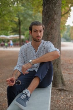 Parma 'daki Ducale parkındaki bankta oturan siyah tişörtlü yakışıklı İtalyan çocuk. Yüksek kalite fotoğraf