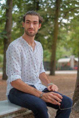 Parma 'daki Ducale parkındaki bankta oturan siyah tişörtlü yakışıklı İtalyan çocuk. Yüksek kalite fotoğraf