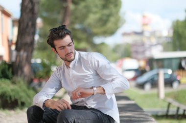 Güzel, siyah saçlı İtalyan çocuk ağaçların altında oturmuş saatini kontrol ediyor. Yüksek kalite fotoğraf