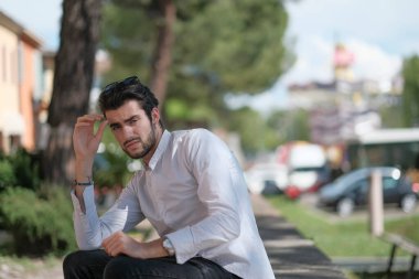 Güzel, siyah saçlı İtalyan çocuk ağaçların altında düşünceli bir şekilde oturuyor. Yüksek kalite fotoğraf