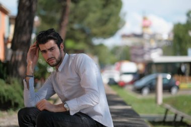 Güzel, siyah saçlı İtalyan çocuk ağaçların altında düşünceli bir şekilde oturuyor. Yüksek kalite fotoğraf