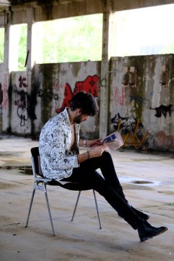 Güzel, siyah saçlı İtalyan çocuk terk edilmiş fabrikada gazete okuyor. Yüksek kalite fotoğraf