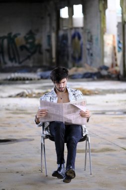 Güzel, siyah saçlı İtalyan çocuk terk edilmiş fabrikada gazete okuyor. Yüksek kalite fotoğraf