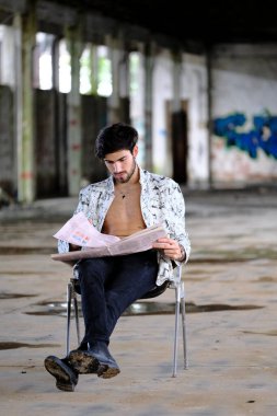 Güzel, siyah saçlı İtalyan çocuk terk edilmiş fabrikada gazete okuyor. Yüksek kalite fotoğraf