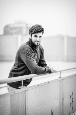 Yakışıklı, siyah saçlı, metal korkuluklara yaslanmış, kırmızı kazaklı bir İtalyan. Yüksek kalite fotoğraf